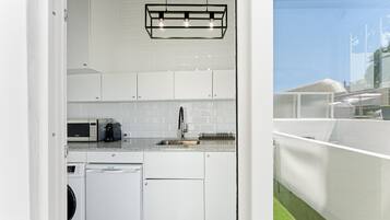 Uma cozinha compacta com armários brancos, micro-ondas embutido, cafeteira e máquina de lavar louça.