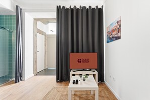 A hotel room with a large window, a flat-screen TV, a small table with a remote, and a door leading to a bathroom. - GuestReady - Peaceful home with a private patio (Porto)
