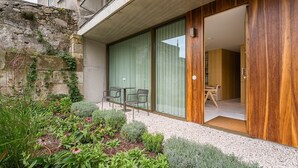 Ein modernes Gebäude mit einer Steinwand, einer Holztür und einer kleinen Terrasse mit Stühlen und Pflanzen.
