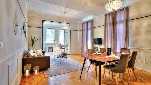 A modern living room with a dining area, featuring a wooden floor, a sofa, a coffee table, and a chandelier.