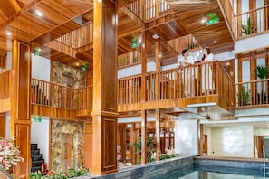 A multi-level wooden interior with a central pool area, wooden railings, and a stone wall. - Mixay Boutique Hotel Da Nang (Da Nang)