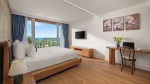 A modern hotel room with a bed, a desk, a chair, a TV, and artwork on the wall.