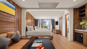 A modern hotel room with a large bed, a sofa, a dining table with apples, and a view of the city.