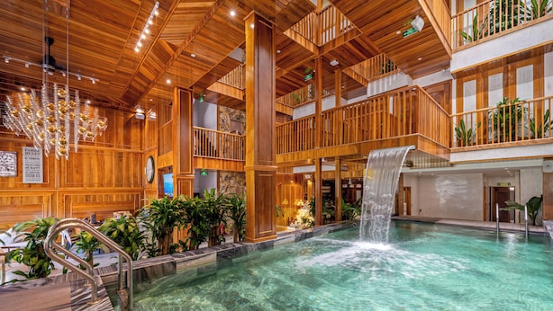 A spacious indoor pool with a waterfall feature, wooden architecture, and multiple levels with balconies.