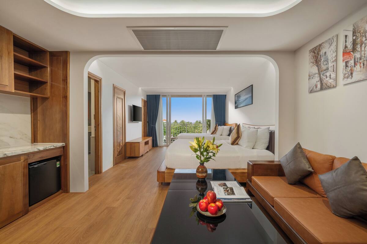 Une chambre d’hôtel moderne avec un plancher en bois, un lit donnant sur un beau paysage, un canapé, une table à manger avec des fruits et un téléviseur.