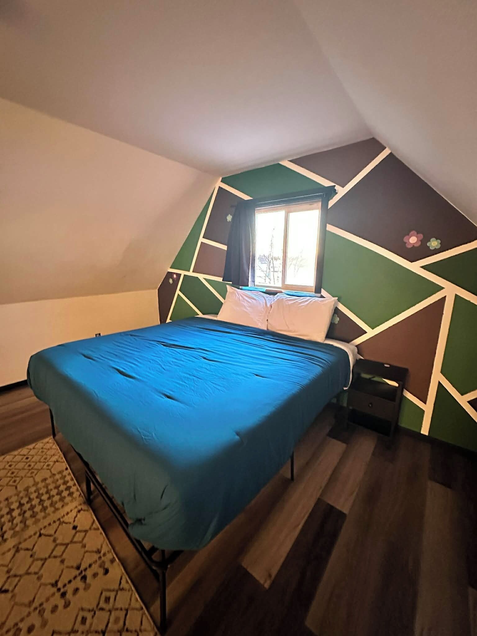 A bedroom with a bed, a window, and a geometric wall design.