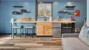 A compact kitchen with a central island, bar stools, a refrigerator, and a microwave. - The Northern Lights Oasis (Wasilla)
