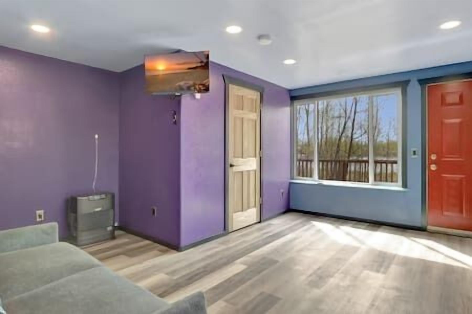 Una stanza con pareti viola, una porta in legno e una finestra che dà su alberi.