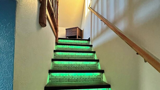 A staircase with green underglow lighting, wooden handrails, and a small wooden table at the top. - The Northern Lights Oasis (Wasilla)