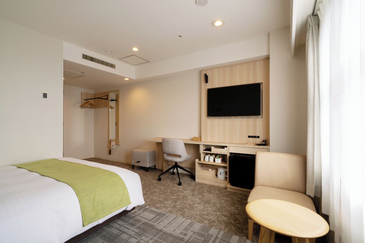 A hotel room with a bed, a desk, a chair, a television, and a wardrobe.