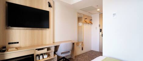 A hotel room with a wooden desk, a flat-screen TV, a chair, a bed, and a wardrobe.