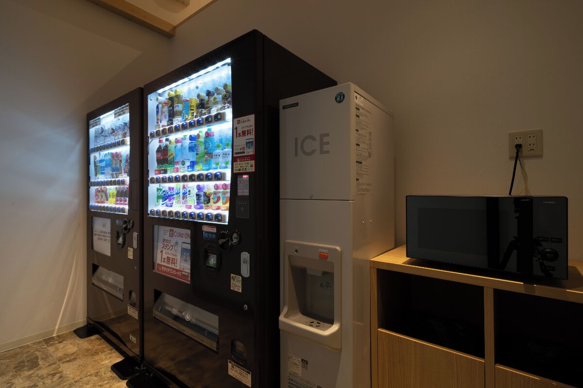 A vending machine area with a refrigerator and a television on a wooden stand.