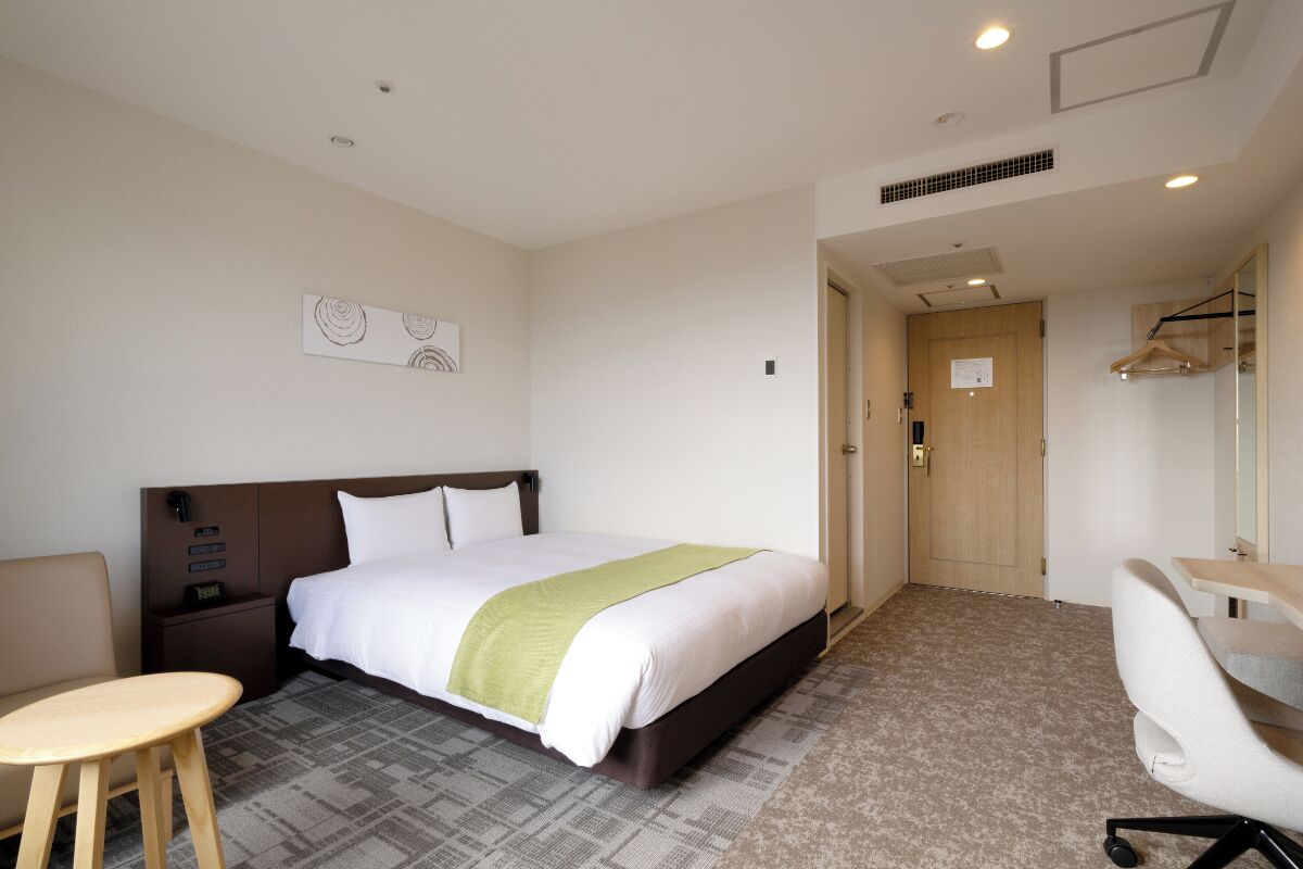 Una habitación de hotel con cama, mesita de noche, silla, escritorio y espejo.