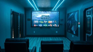Ein Star Wars-zimmer mit großem Bildschirm, der die Filmreihe zeigt, Holzboden und einer Sitzecke mit Stühlen.