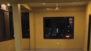 A spacious room with a large window, a ceiling fan, and two yoga mats on the floor. - Hotel August International (Pokhara)