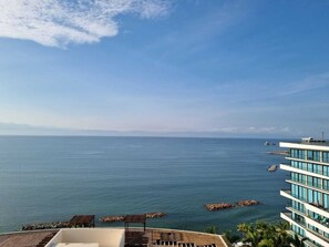 A coastal view with a clear sky, calm sea, and a modern building with multiple balconies overlooking the water.
