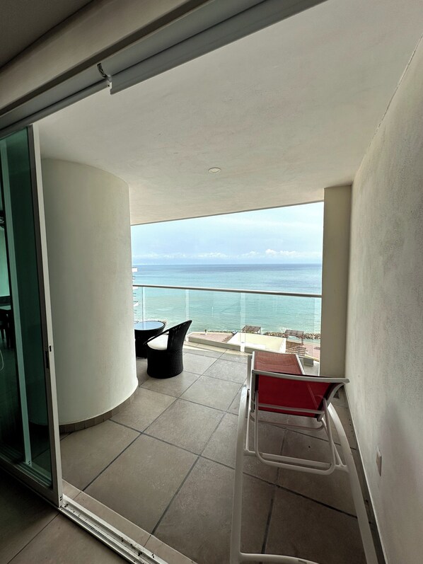 Un balcón con vista al mar, una puerta de cristal y una silla roja.