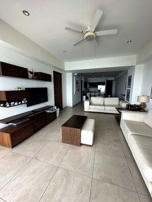 A modern living room with a flat-screen TV, dark wood entertainment unit, a white sofa, a coffee table, and a ceiling fan.