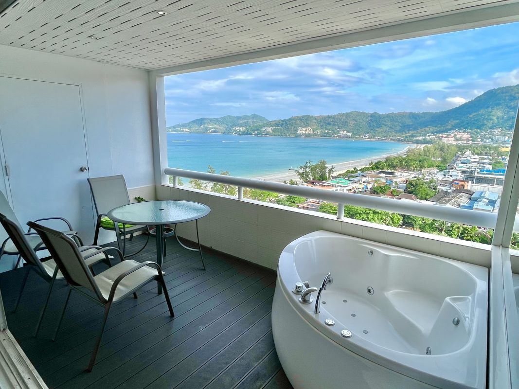 A balcony with a view of the sea, a round table, two chairs, and a large bathtub.