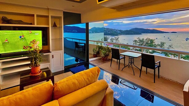 Una sala de estar moderna con un televisor grande, un sofá amarillo y un balcón con vistas al mar.