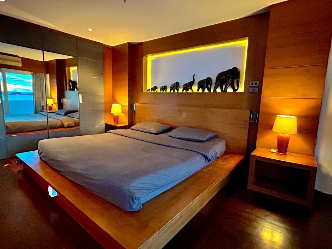 A modern hotel room with a large bed, a wall-mounted elephant sculpture, and a mirror reflecting the room.