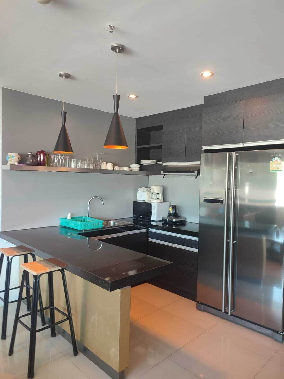A modern kitchen with a central island, stainless steel appliances, pendant lighting, and a dark cabinetry design.