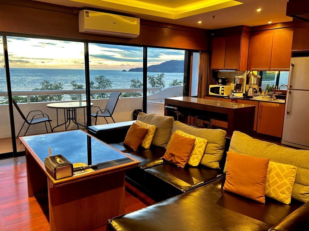 Una sala de estar moderna con un sofá, una mesa de centro y vista al mar. Hay una zona de cocina con microondas y refrigerador.