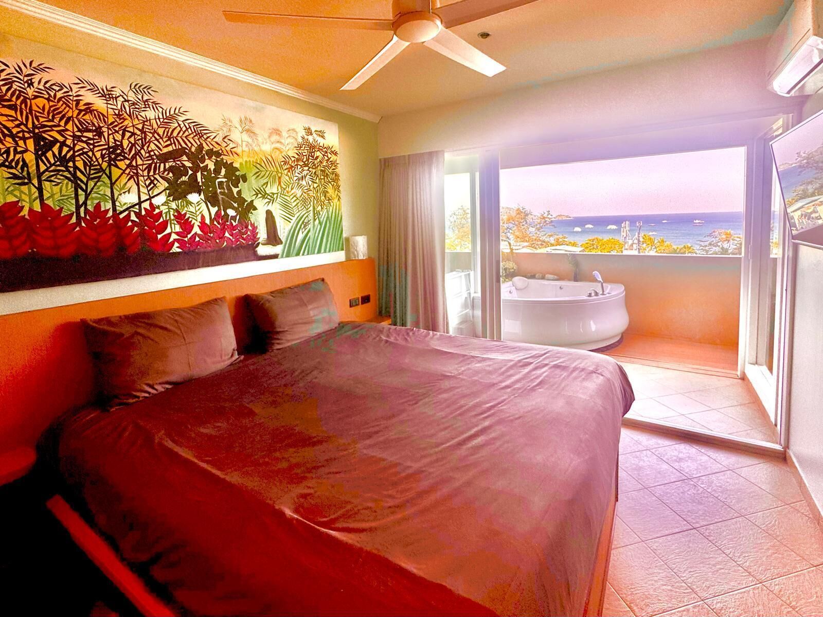 Une chambre dotée d’un grand lit, d’un ventilateur de plafond, d’un tableau et d’un balcon avec un jacuzzi.
