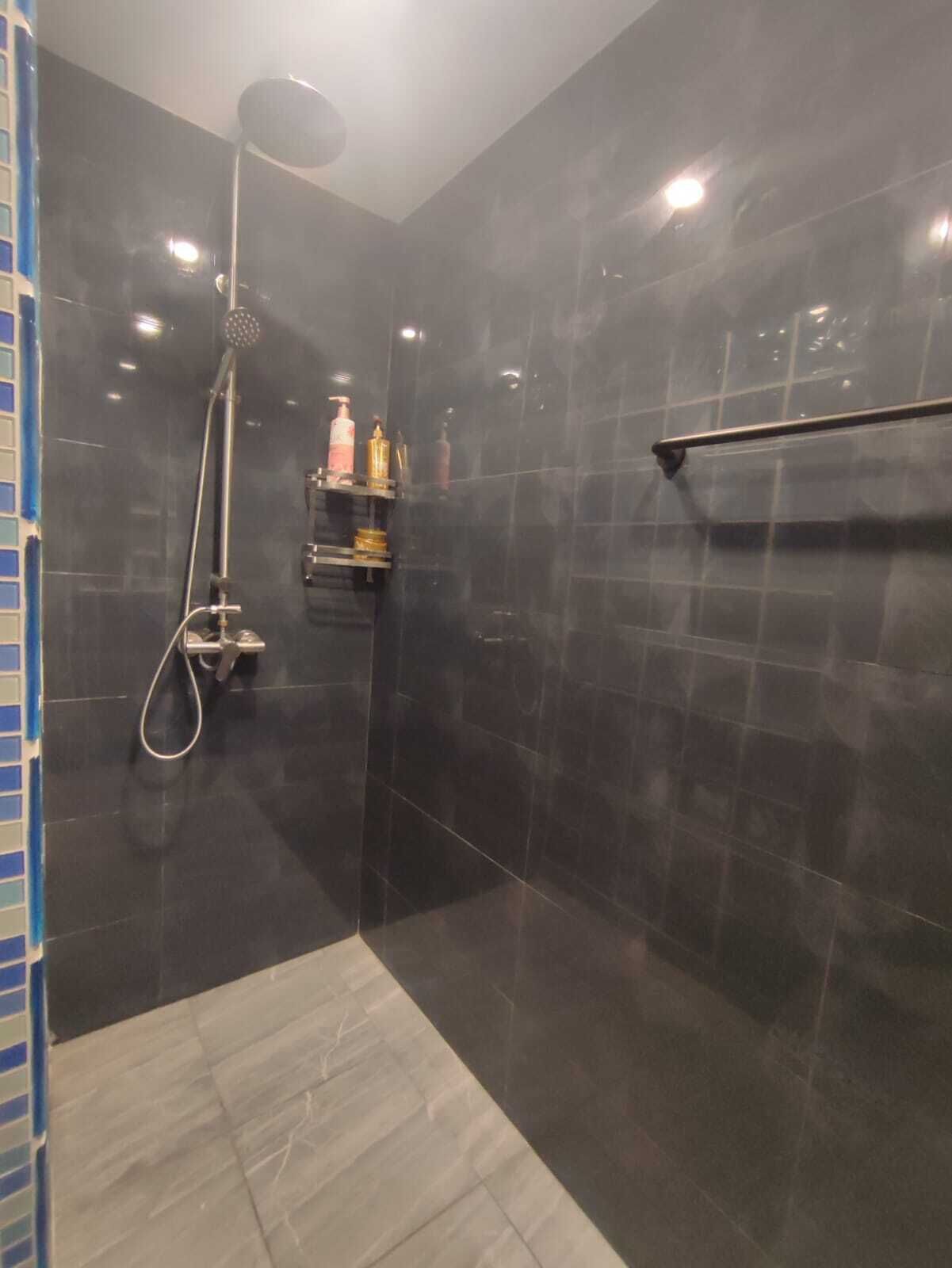 A modern bathroom with dark tiles, a shower, and a shelf with toiletries.