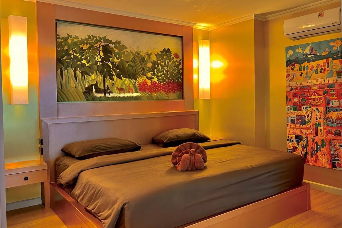 Ein Schlafzimmer mit einem großen Bett, zwei Nachttischen, einem Gemälde über dem Bett und einer Klimaanlage an der Wand.
