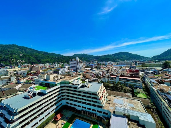 Um hotel moderno com vários andares, piscina no terraço e vista para a paisagem urbana e as colinas ao redor.