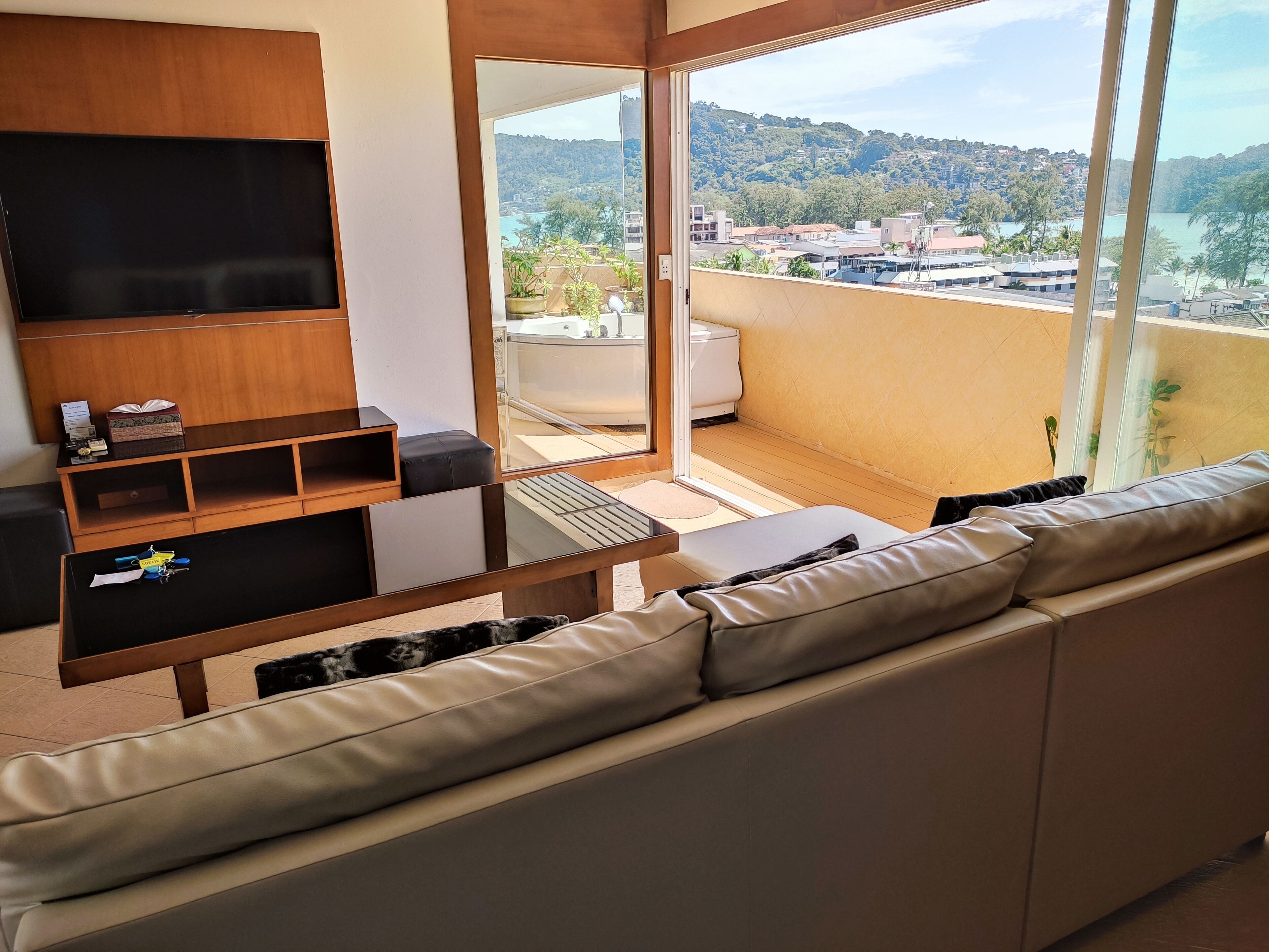 Una sala de estar moderna con un sofá, un televisor y un balcón con vistas a un paisaje urbano.