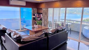 Una habitación de hotel moderna con un balcón grande, sofás de cuero, una mesa de centro de madera y vista al mar.