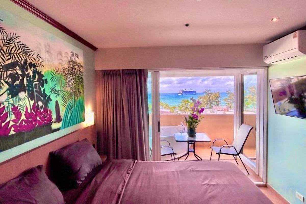 A hotel room with a bed, a balcony with a table and chairs, and a view of the sea.