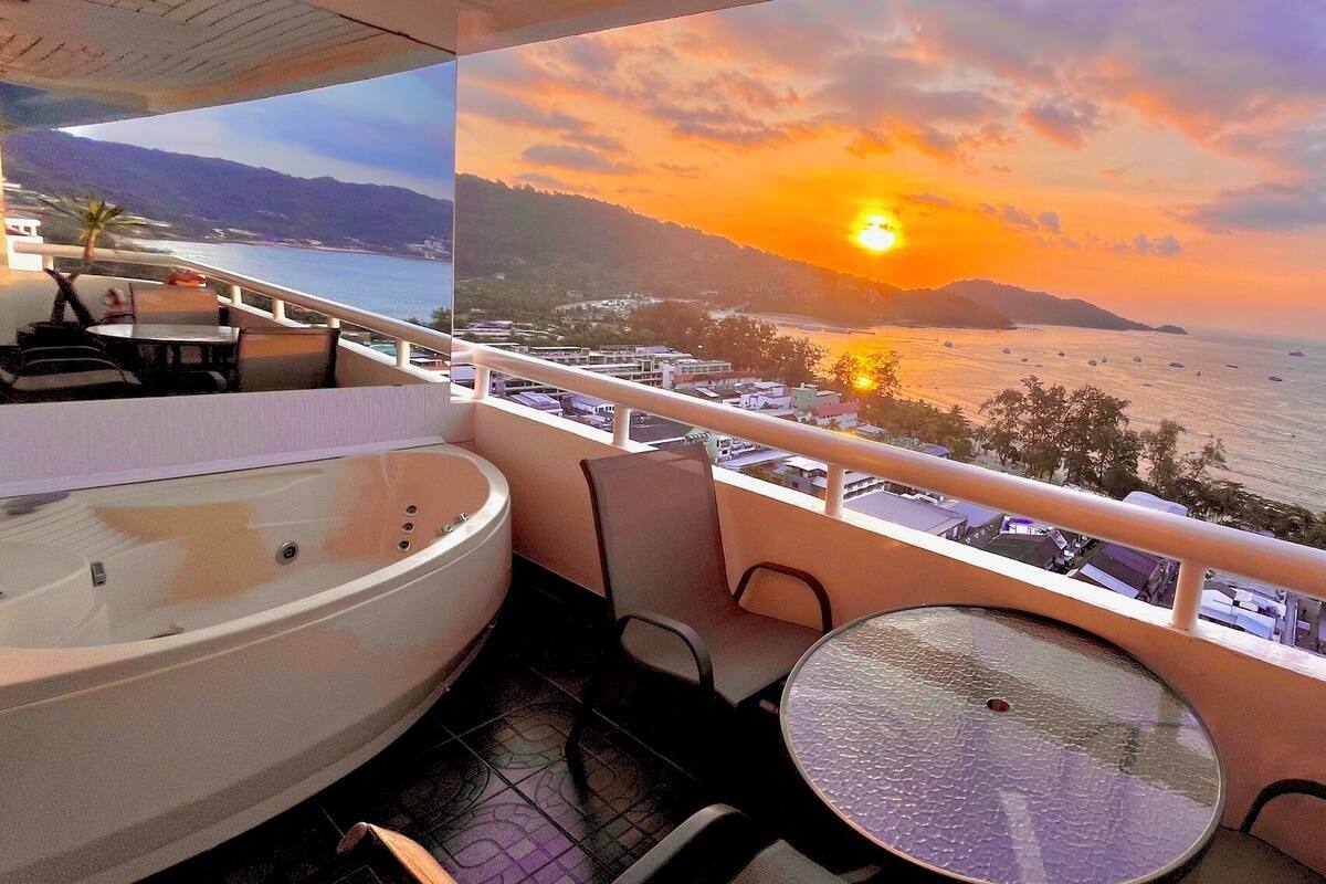 Ein Balkon mit Whirlpool, Tisch und Stühlen mit Blick auf einen Küsten-Sonnenuntergang.