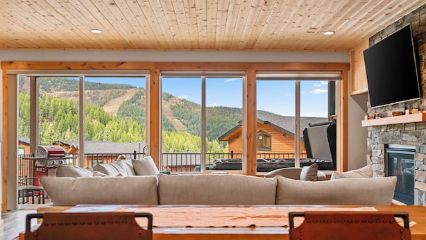 A spacious living room with a large sofa, a dining table, and a stone fireplace. - Schweitzer Lux Powder Dreams I Hot Tub I Families (Sandpoint)
