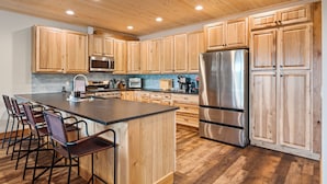 A modern kitchen with wooden cabinets, stainless steel appliances, and a central island with bar stools. - Schweitzer Lux Powder Dreams I Hot Tub I Families (Sandpoint)