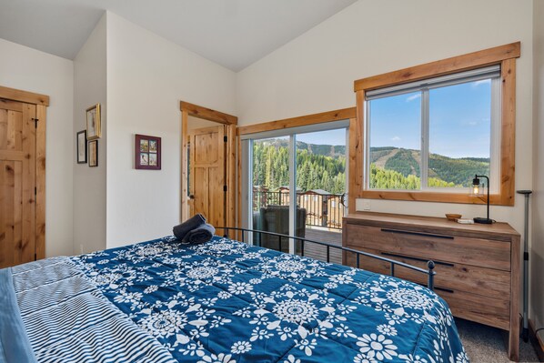 A bedroom with a large bed, wooden dresser, and a window with a mountain view.