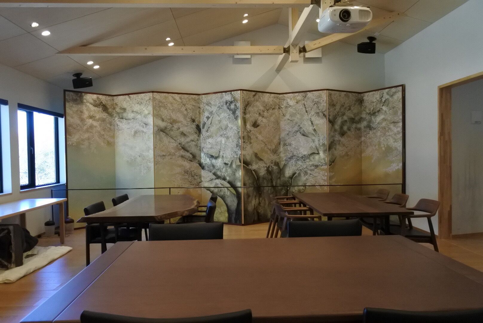 A conference room with a large table, chairs, a projector, and a screen.