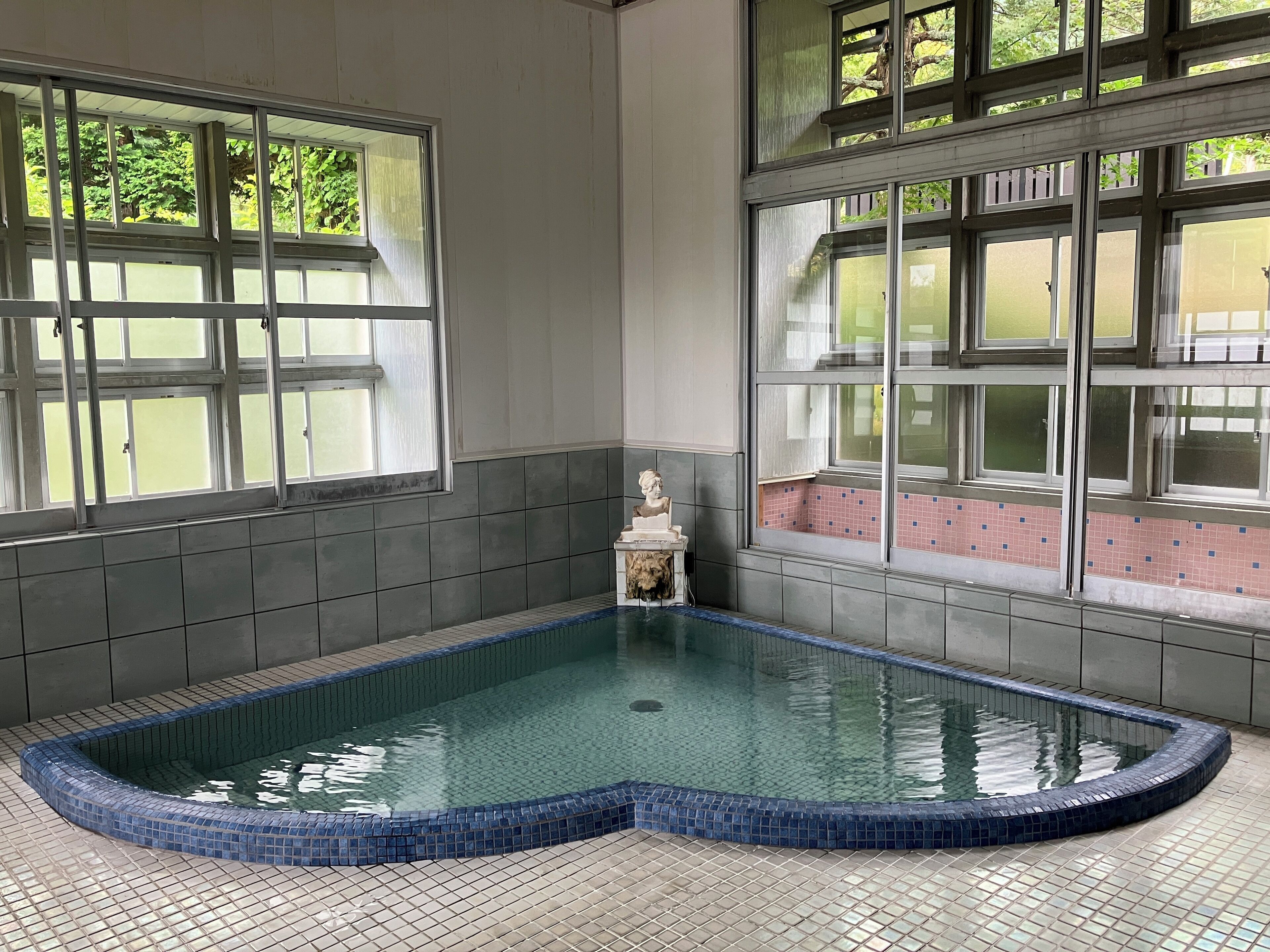 A swimming pool with a tiled edge, large windows, and a statue in the corner.