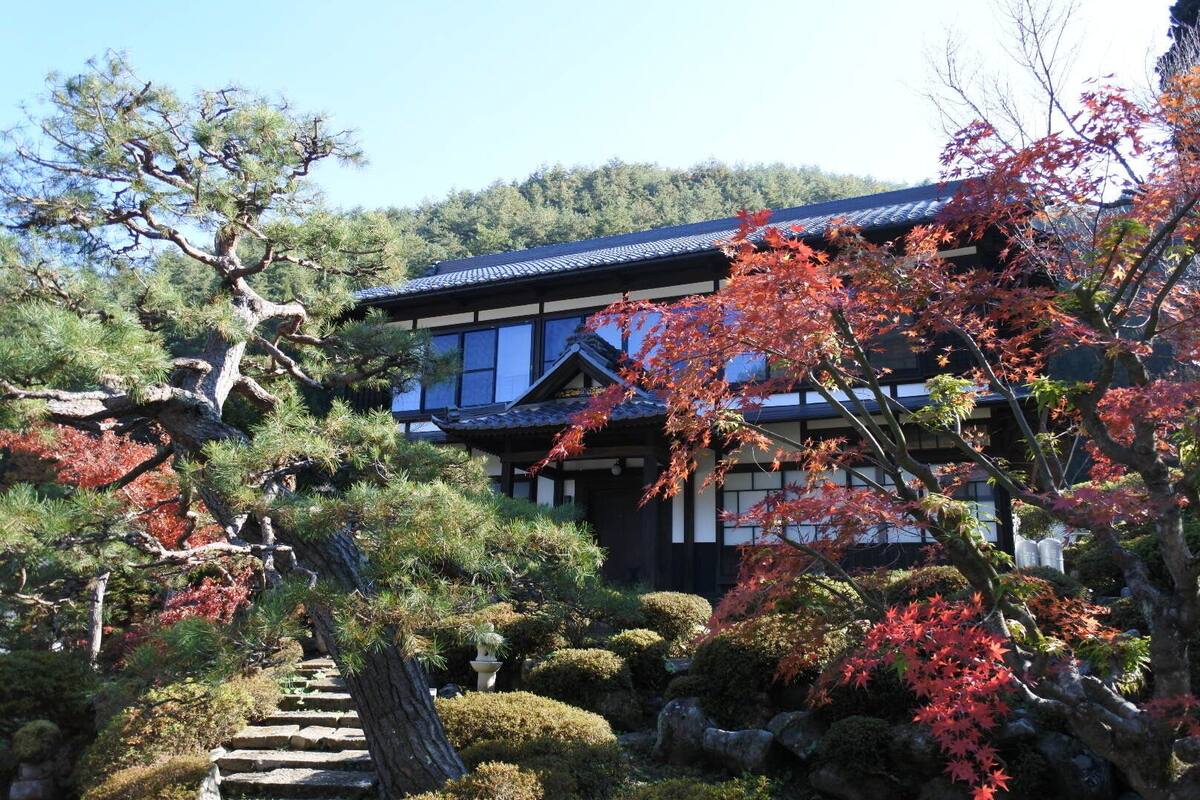A traditional Japanese building with a tiled roof, surrounded by a garden with various trees and shrubs.