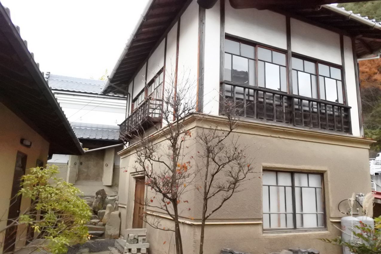 A traditional Japanese building with a tiled roof, a balcony, and a stone statue in the courtyard.