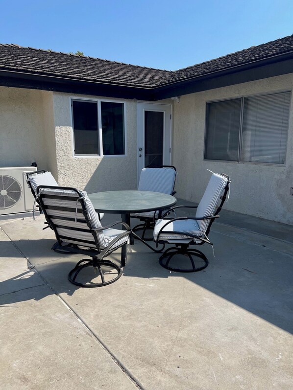 An outdoor patio with a round table and four chairs, a window, and an air conditioning unit.