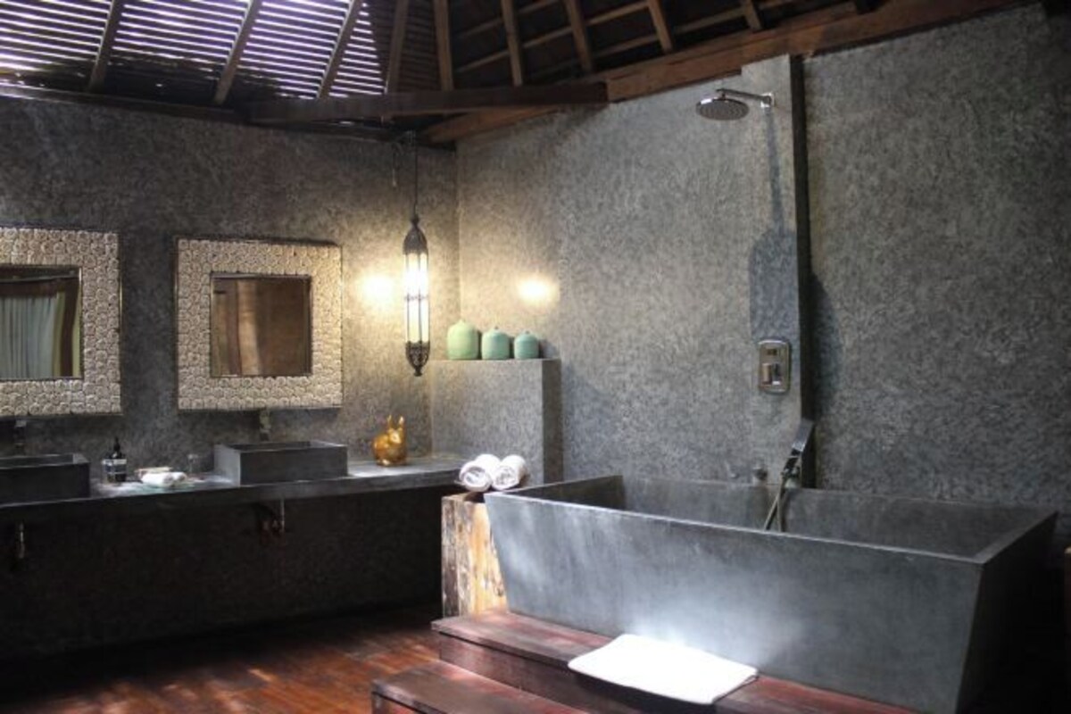 A modern bathroom with a large bathtub, a wooden bench, and a stone wall.
