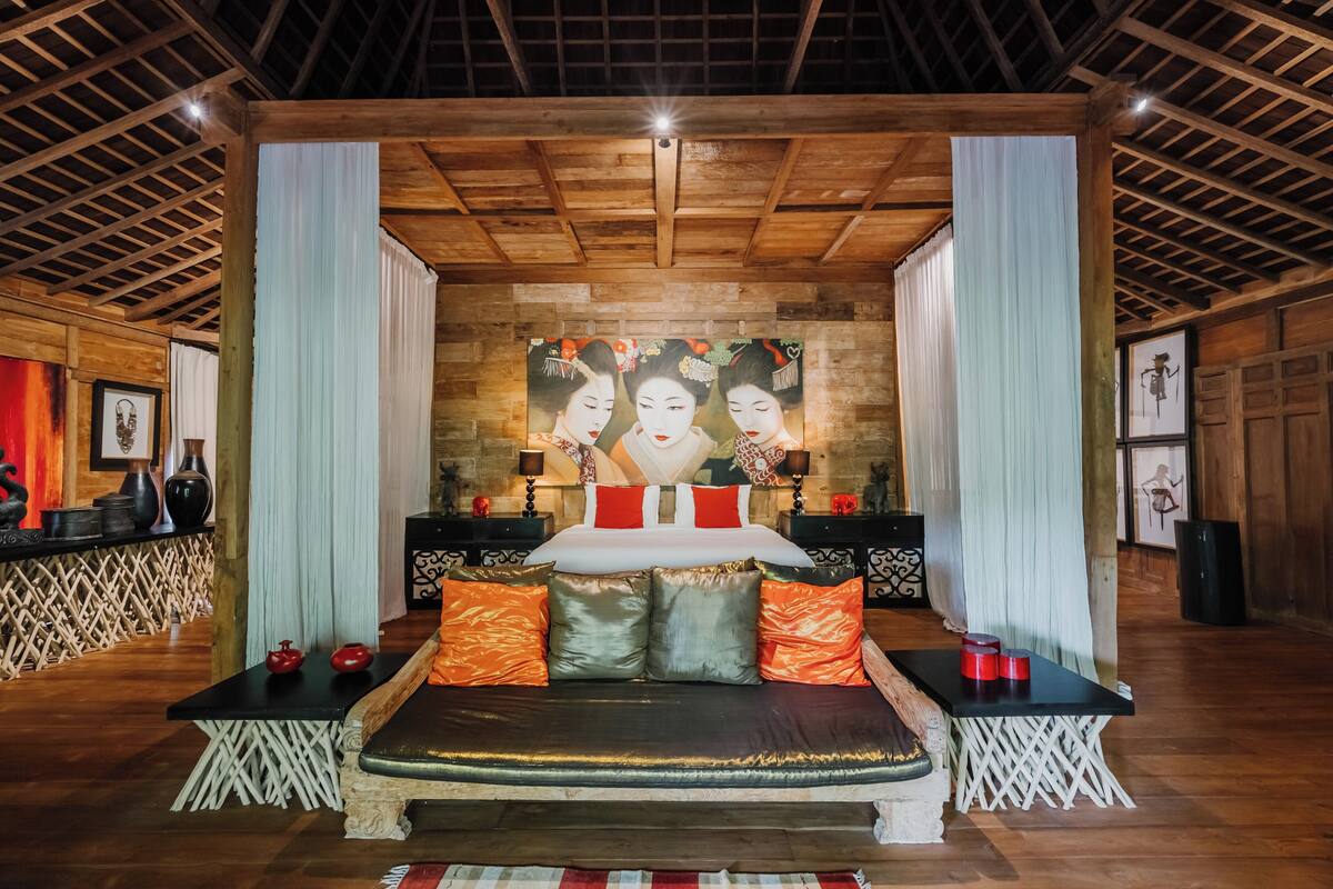 A traditional-style bedroom with a large bed, wooden beams, and a mural on the wall.