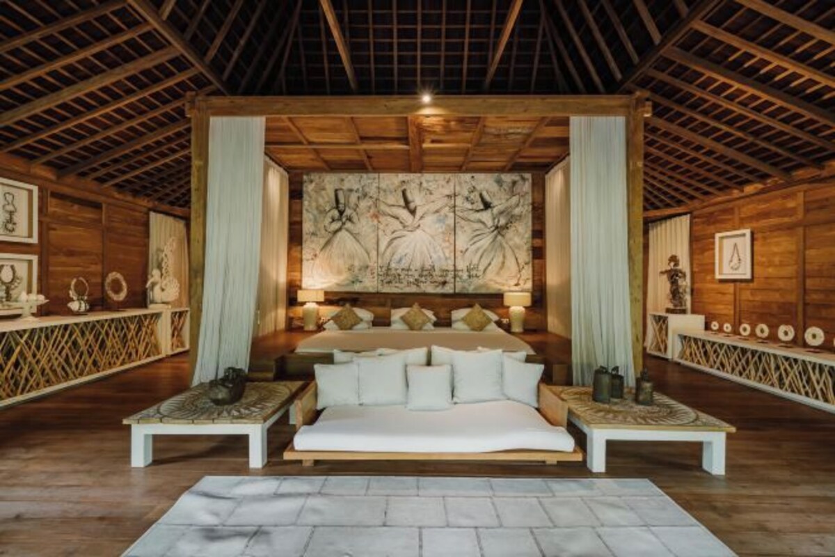 A spacious bedroom with a large bed, two nightstands, a wooden ceiling, and a large artwork on the wall.
