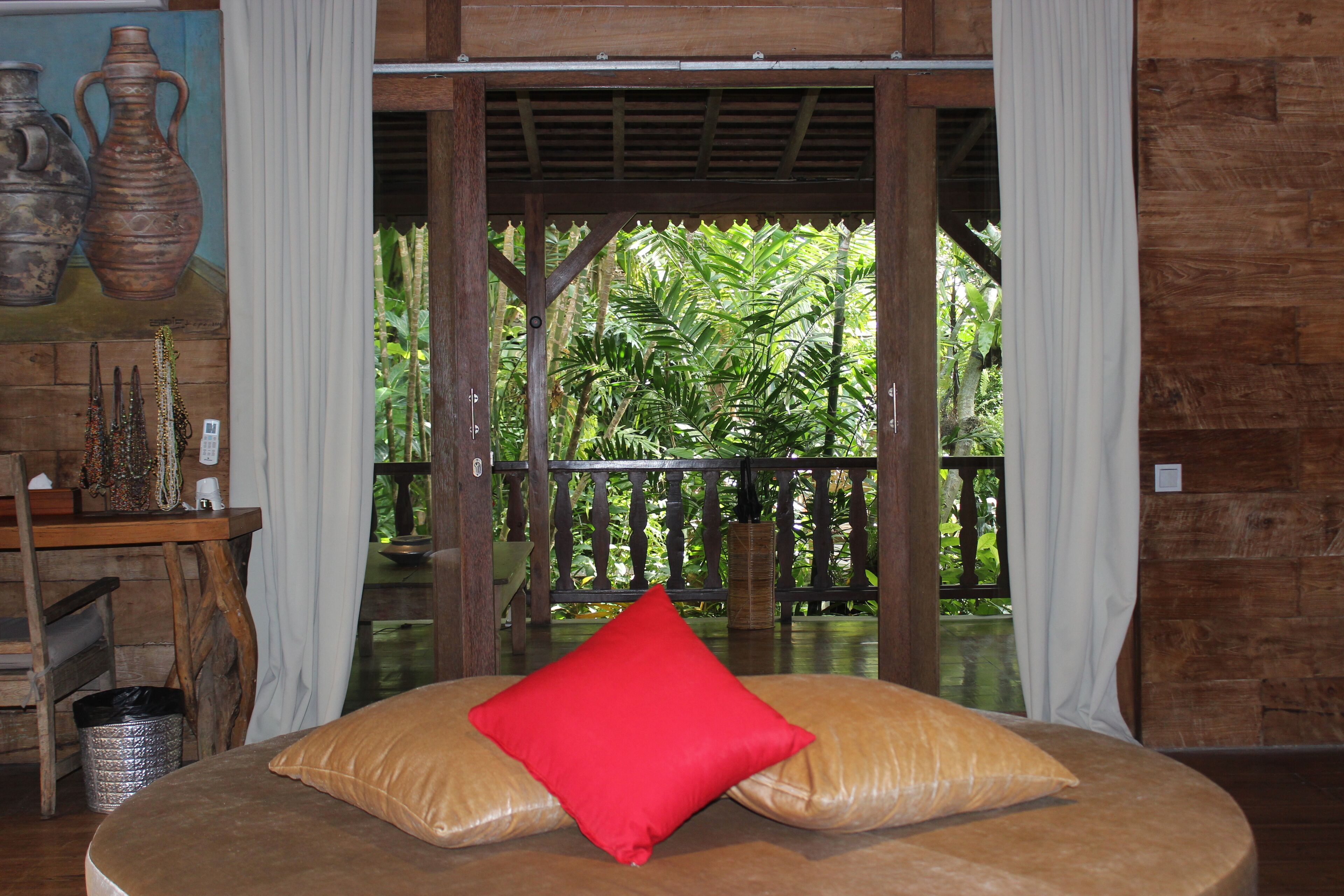 A room with a bed, a red pillow, and a view of greenery outside.