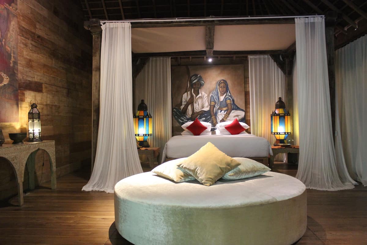 A bedroom with a round bed, white curtains, and two wall-mounted lamps.