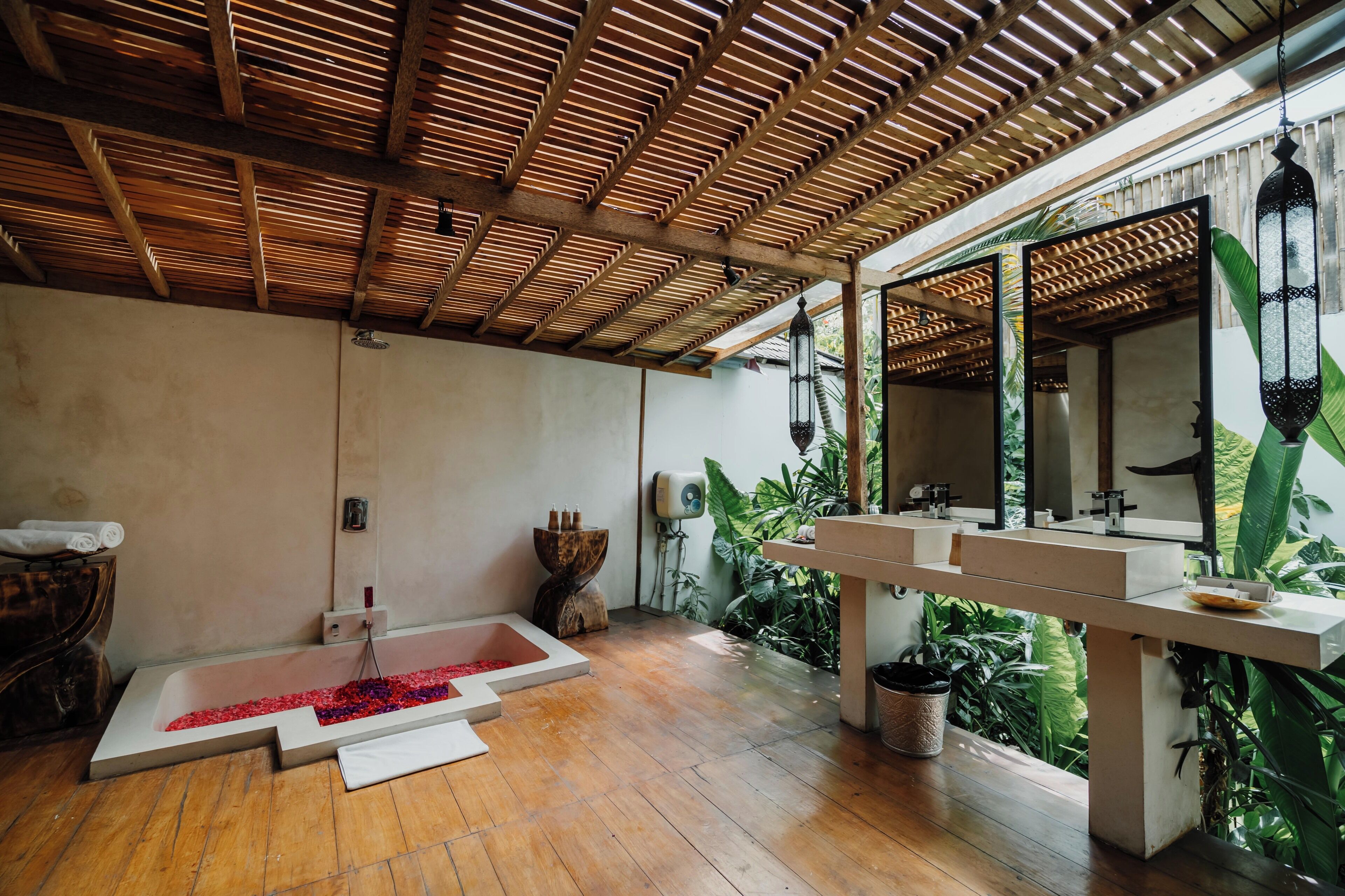 Un baño con techo de madera, una bañera con flores rojas, un mueble de madera y un espejo grande.