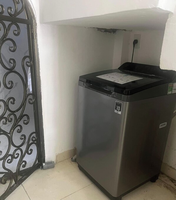 A compact, stainless steel trash bin with a black lid, placed in a corner next to a white wall and a decorative metal gate. - Motel Mys Dung as  Motel Lavie  (Tay Nha Trang)